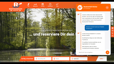 Screenshot der Website „Bootsverleih Richter“ mit eingeblendetem KI-Chatbot. Im Chat fragt ein Nutzer, ob Hunde zum Paddeln mitgenommen werden dürfen. Der Chatbot antwortet, dass Hunde grundsätzlich erlaubt sind, die Mitnahme von der Größe abhängt und für größere Hunde ein kippstabiles 3er-Kanadier empfohlen wird. Im Hintergrund ist eine bewaldete Flusslandschaft mit einem Kajak zu sehen.