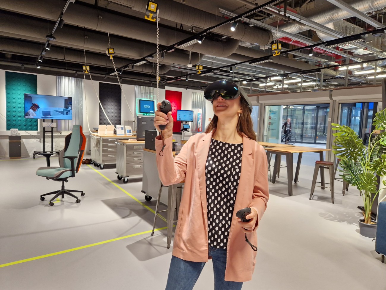 Eine Frau trägt eine Virtual Reality-Brille und benutzt zwei Controller, während sie sich dabei durch einen Raum bewegt.